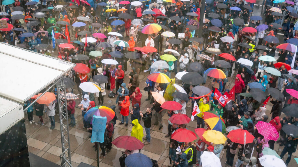 Große Menschenmenge mit Regenschirmen vor dem Erwin-Piscator-Haus